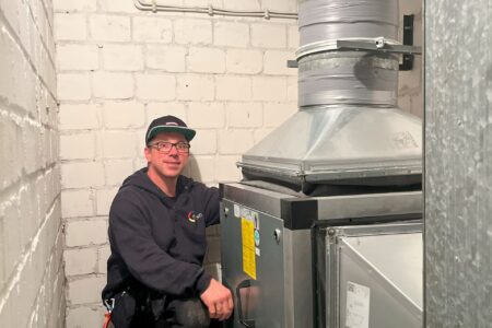 Fachhandwerker bei Wartungsarbeiten an einer zentralen Lüftungsanlage mit großem Luftkanal im Technikraum.