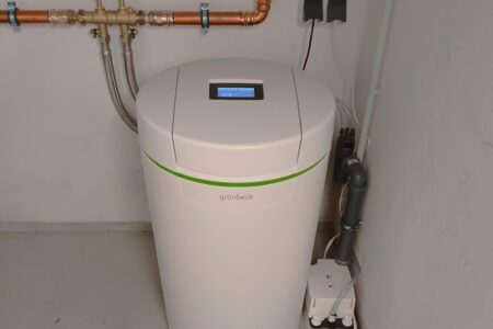 Installierte Grünbeck Wasserenthärtungsanlage mit Kupferleitungen und Anschlüssen in einem Technikraum.
