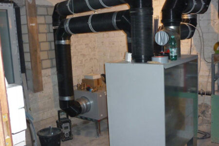 Zentrale Lüftungsanlage mit groß dimensionierten schwarzen Luftkanälen bei der Installation in einem Kellerraum